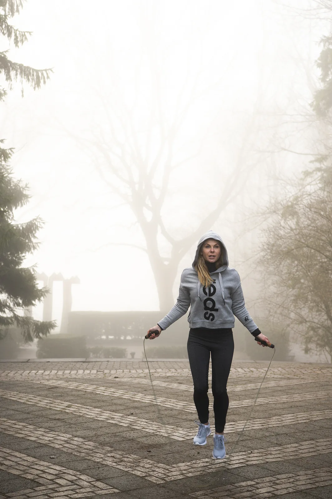 Barbara jumping rope outdoors in a foggy park, mid-workout