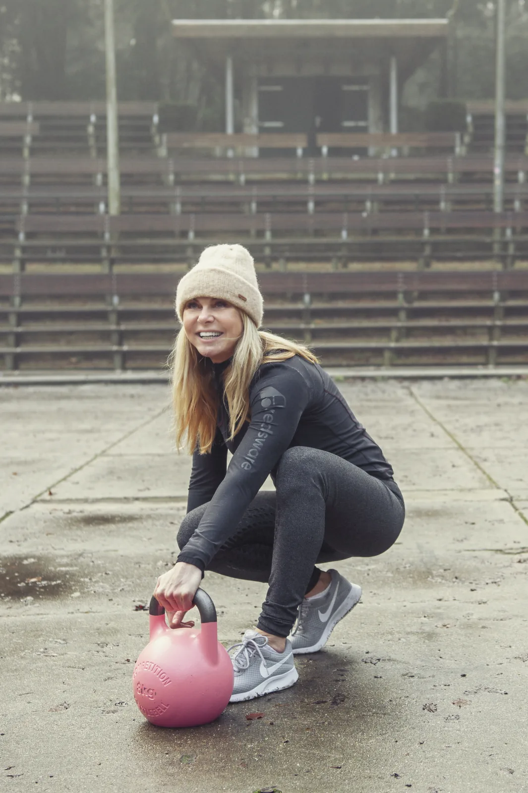 Barbara Rubin smiling mid-workout outdoors, crouched down beside a kettlebell
